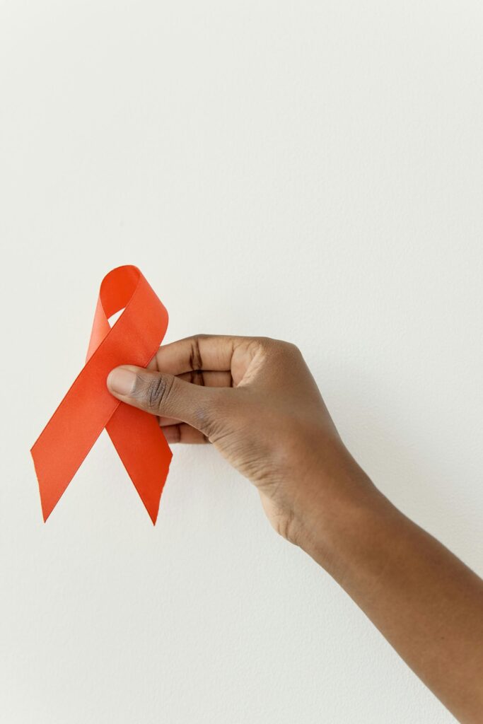 A hand holding a red awareness ribbon on a white background symbolizing cancer awareness.